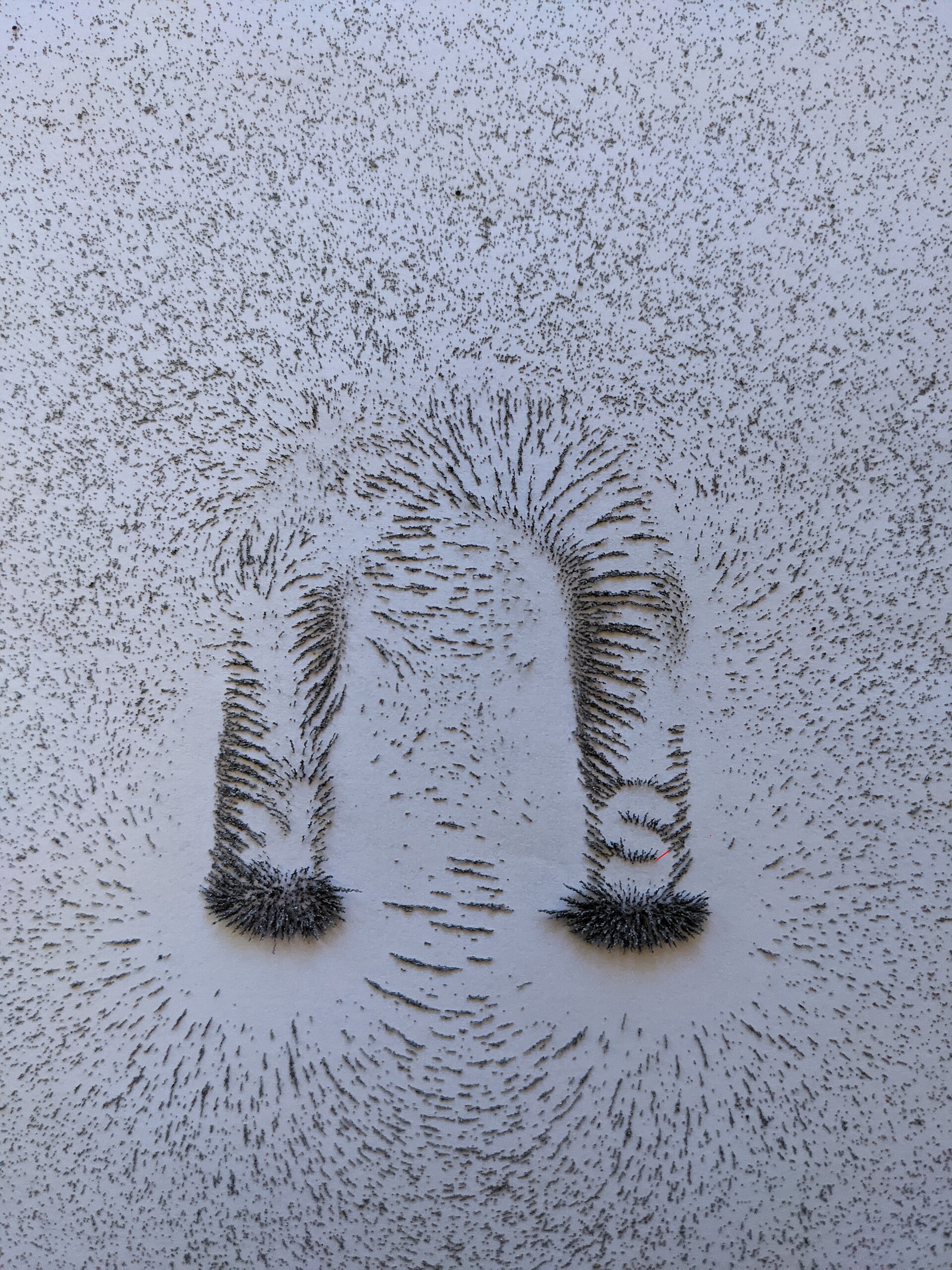 A horseshoe magnet under paper pulling iron filings into lines
